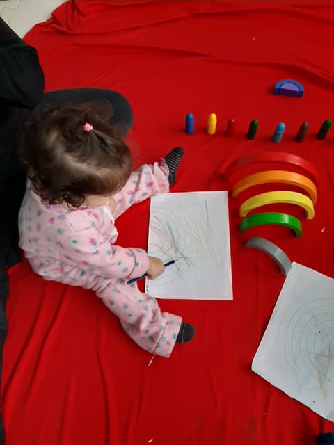 Criança desenhando com giz de cera ao lado de blocos coloridos