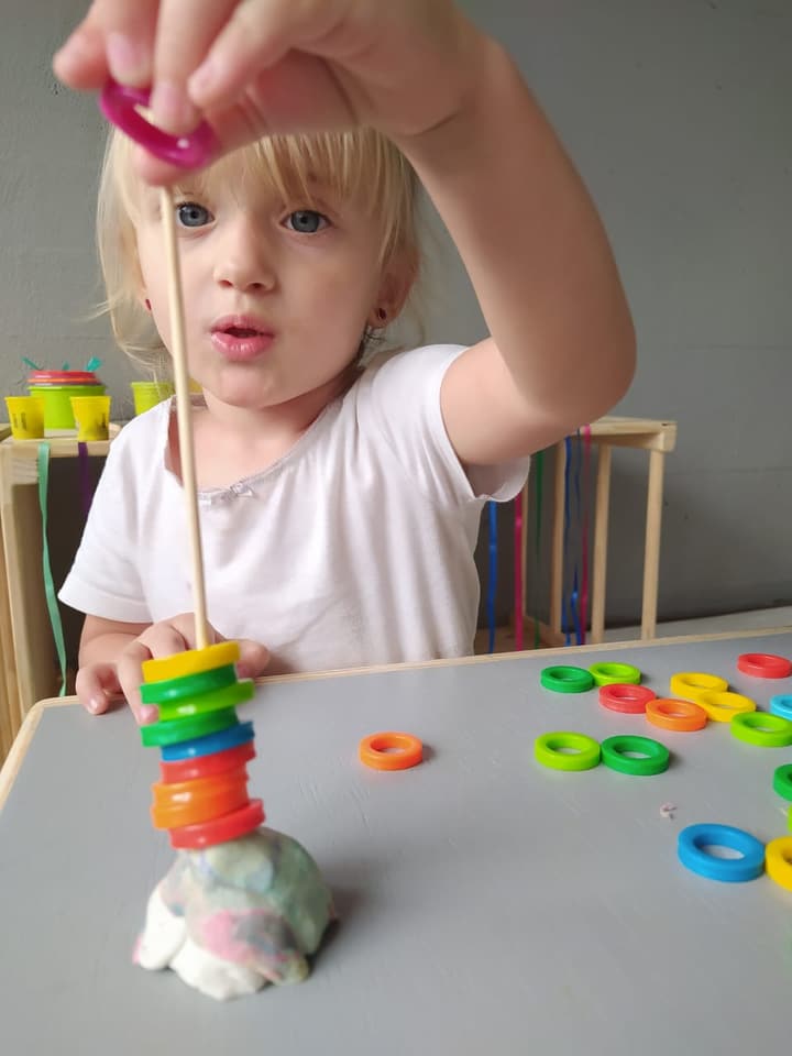 Criança empilhando argolas coloridas com massinha